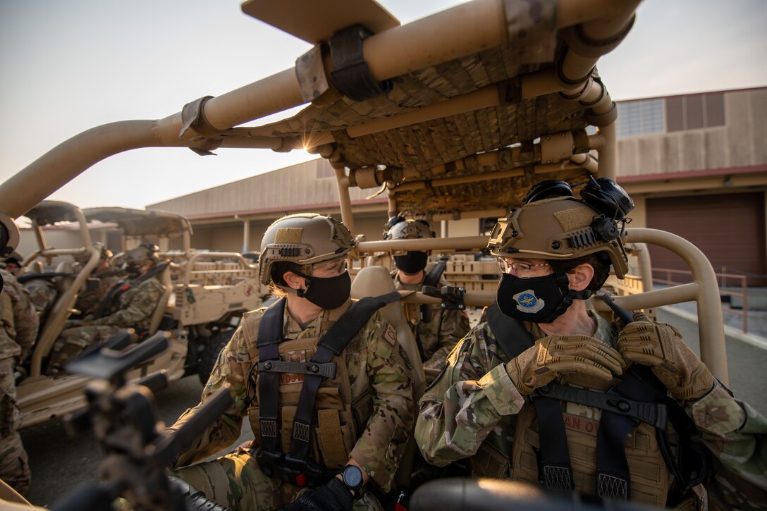 Two military members sit in an open-air buggy vehicle of sorts with masks on.