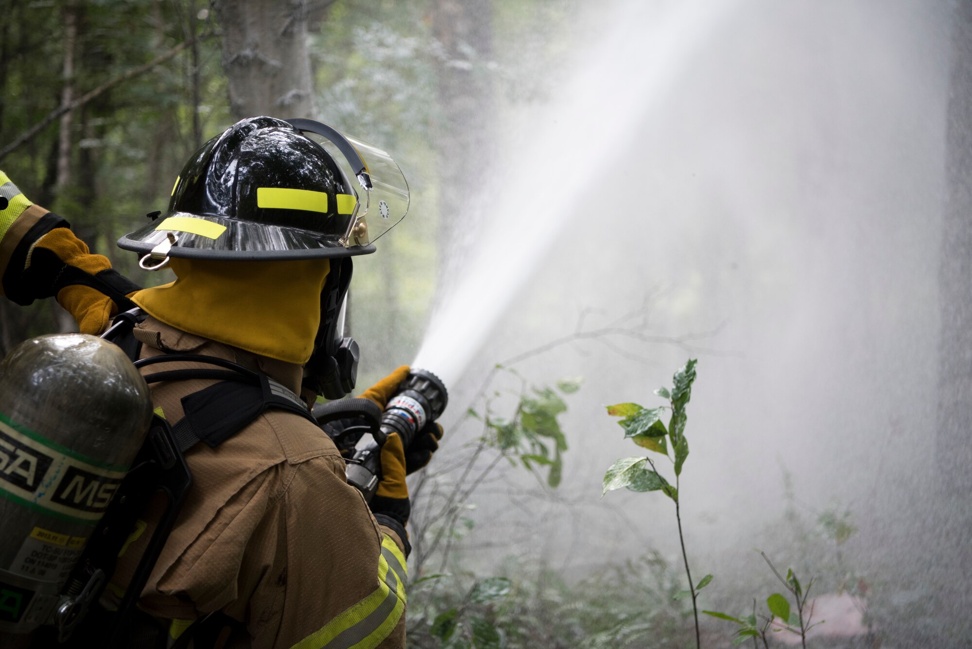 Firefighter sprays water onto simulated aircraft crash.