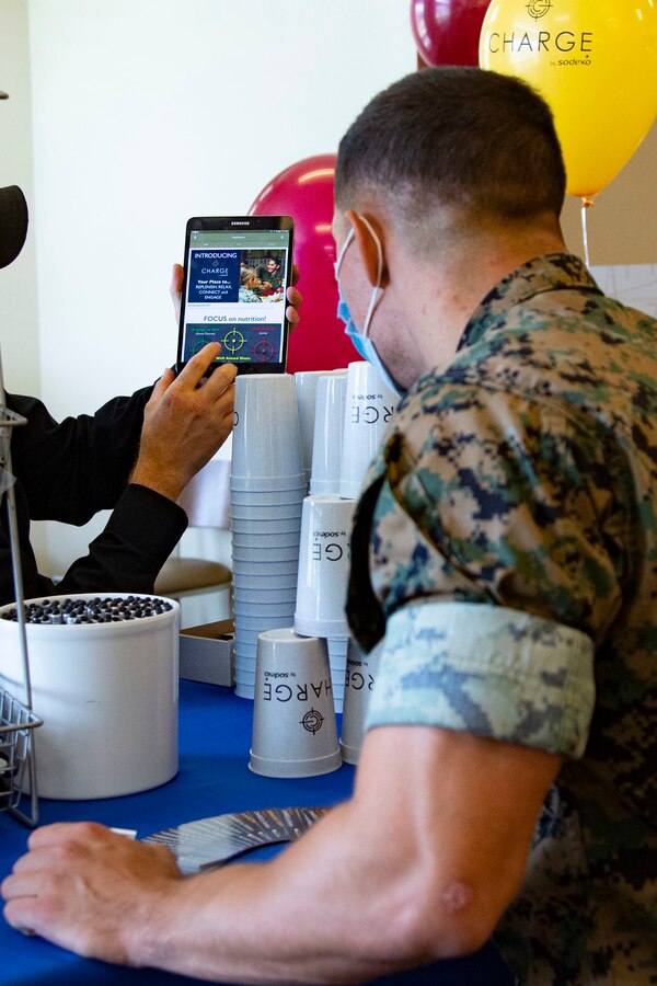Allen Wolff, left, an information technology specialist for Sodexo, guides a U.S. through the set up process of the newly released mobile app, Charge by Sodexo, during the app’s launch event at the French Creek 65 Mess Hall on Marine Corps Base Camp Lejeune, North Carolina, Aug. 24, 2020. Charge by Sodexo is a free mobile app available on the Google Play Store and Apple App Store and features mess hall searching capability through geo-location or installation name and mess hall number which allows users to view local menus for specialty bars, caloric intake information, nutrition facts and feedback.  (U.S. Marine Corps photo by Lance Cpl. Ginnie Lee)