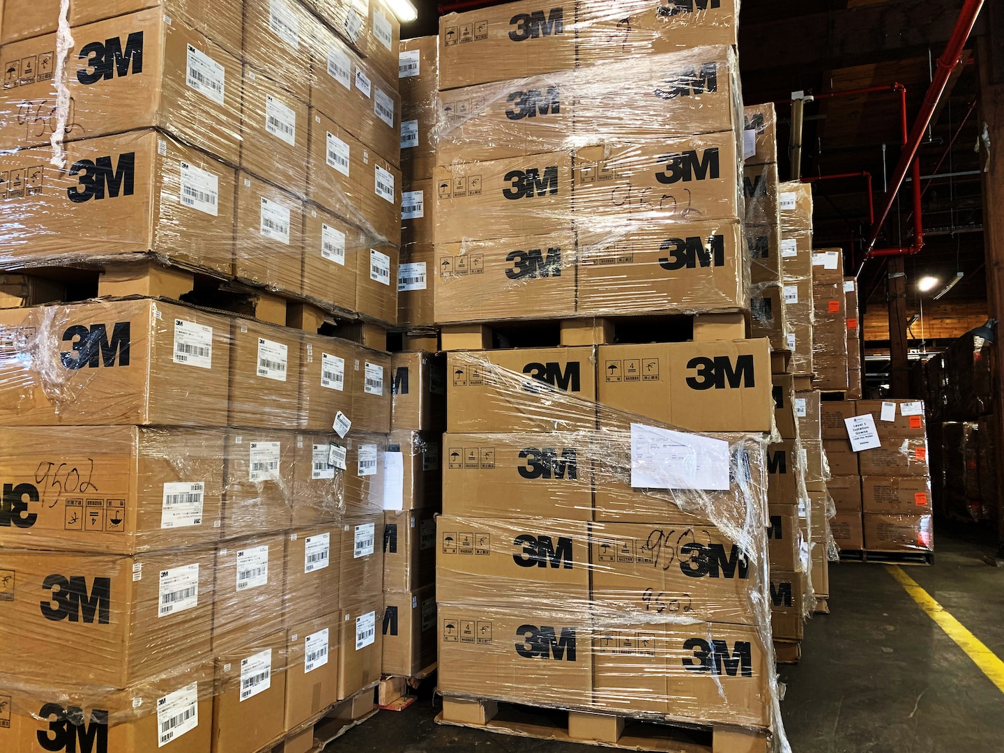 Boxes labelled 3M, shrink wrapped, and stacked on pallets in a warehouse