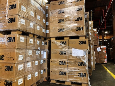 Boxes labelled 3M, shrink wrapped, and stacked on pallets in a warehouse