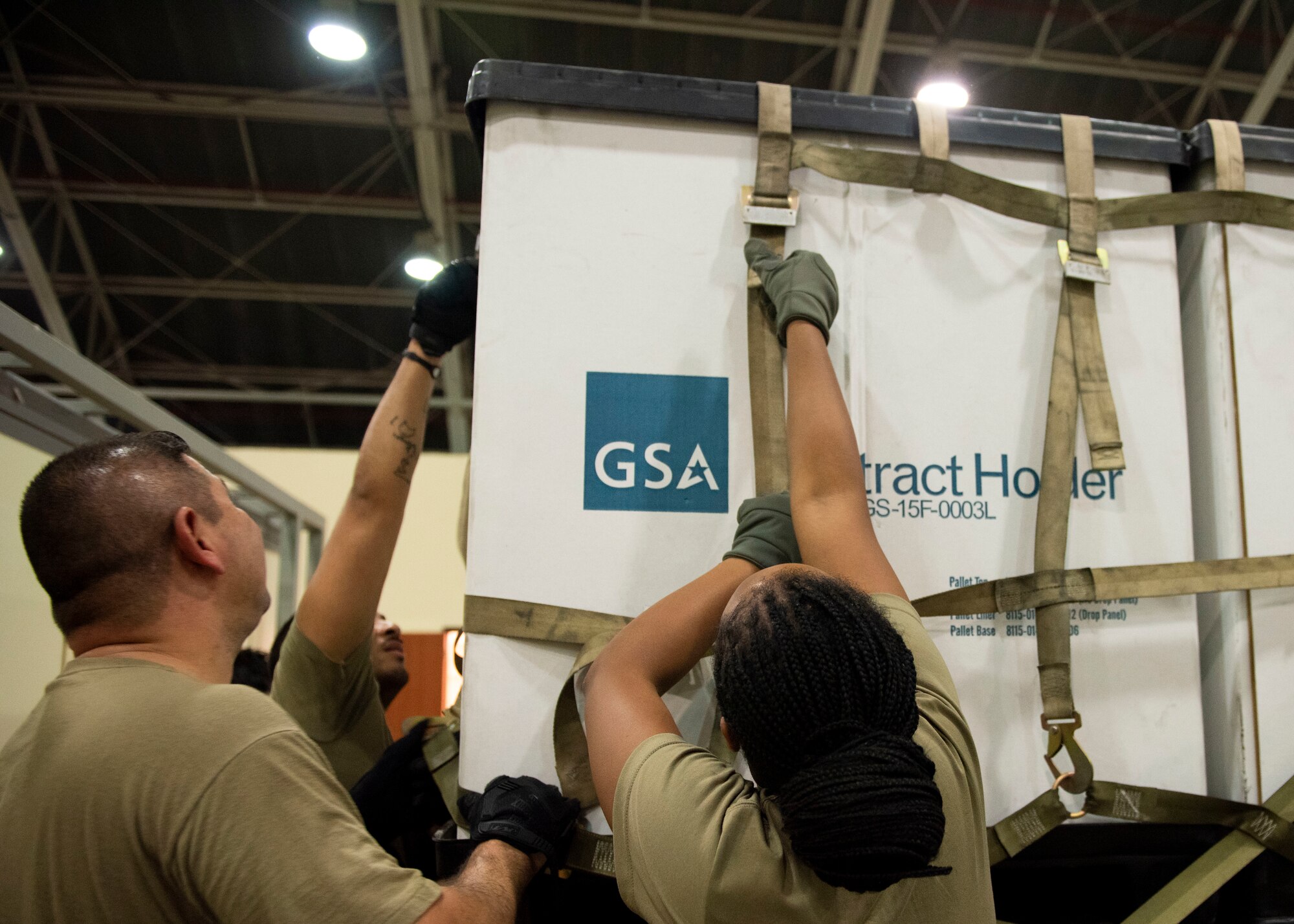 Airmen work together to tighten a cargo net over a large pile of cargo containers.