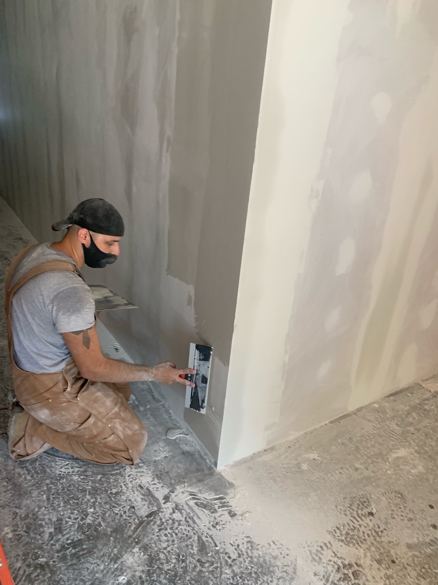 Worker sits on floor making repairs to hole in a wall.