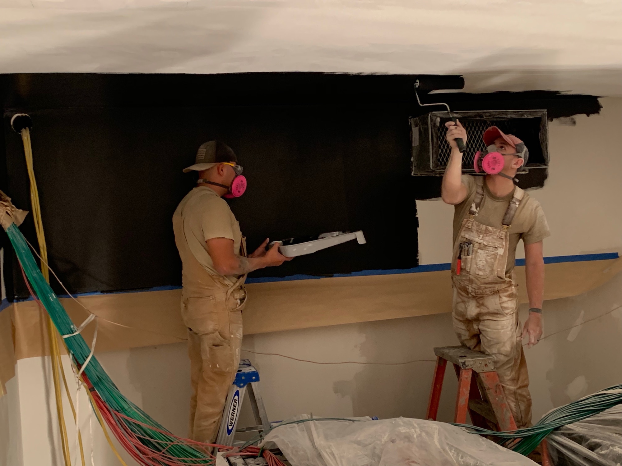 Two workers standing under ceiling making repairs.