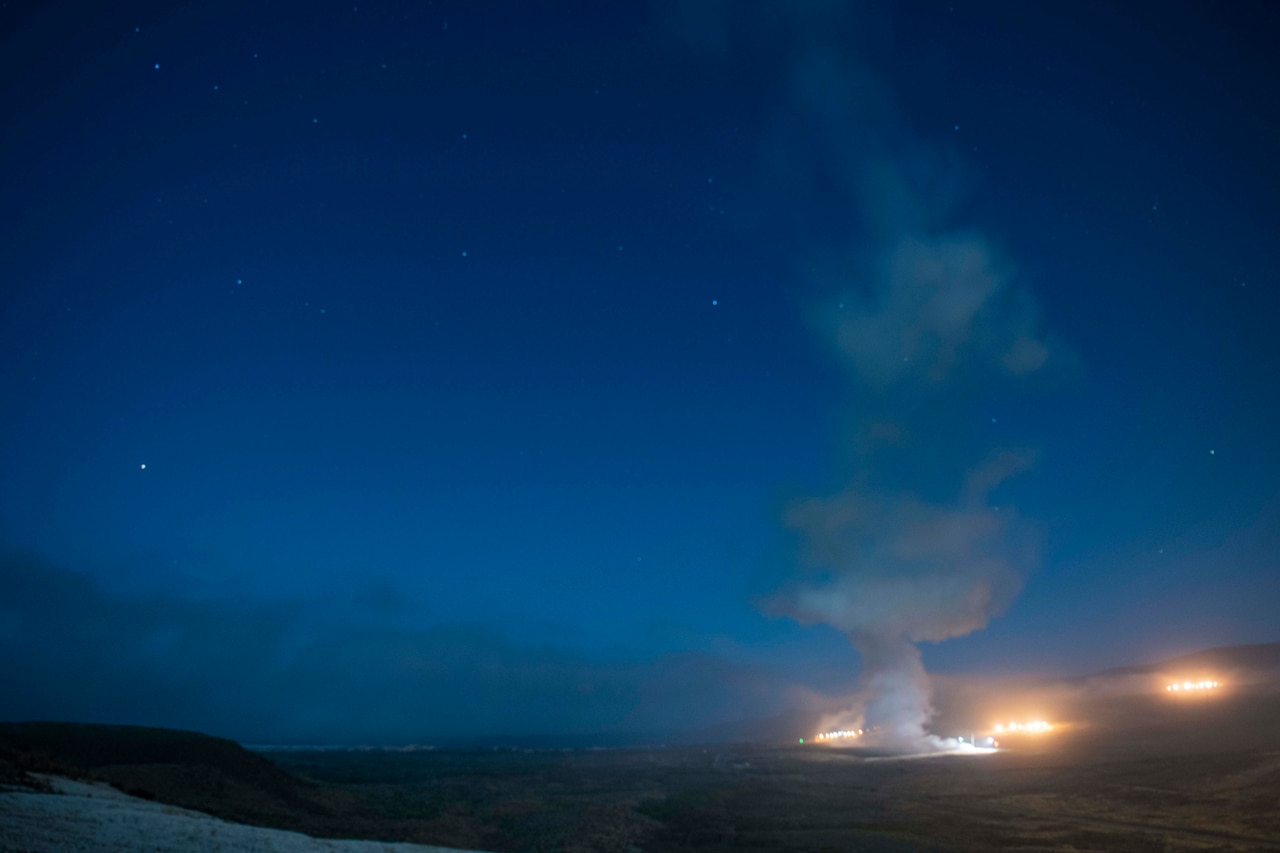 Lights and a plume of smoke can be seen against a dark sky.
