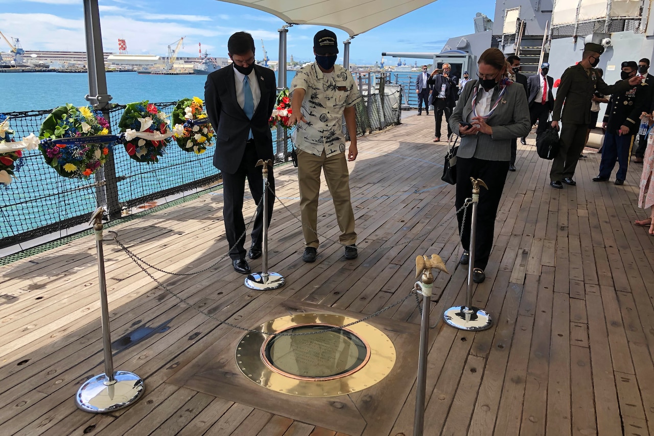 Three people examine a plaque set into the deck of a ship.