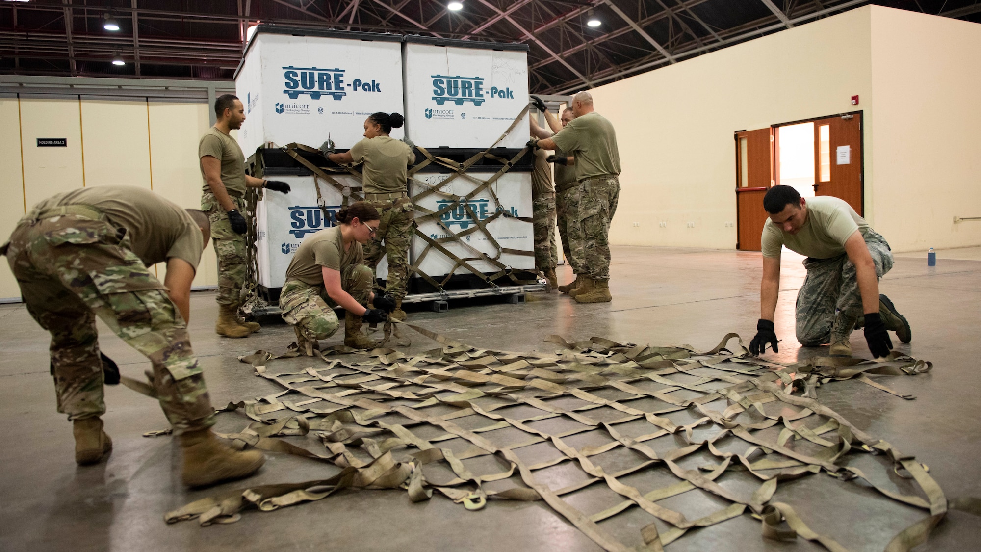 Airmen prep a cargo net on the floor of a warehouse before putting it onto a aircraft sized cargo pallet at Incirlik Air Base.