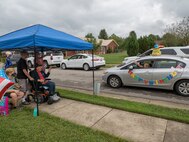 line of cars drives past a group of people.