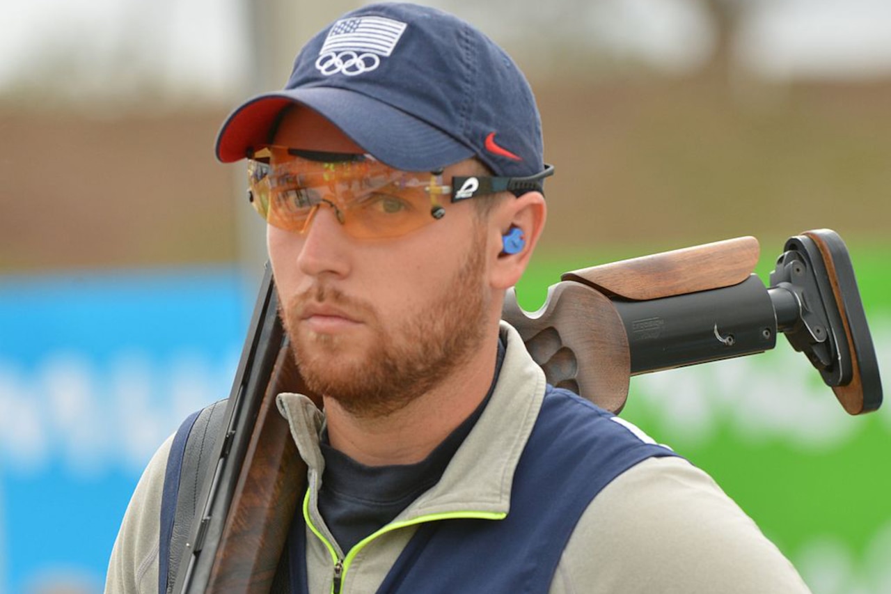 A man holding a shotgun over his shoulder poses for a photo.