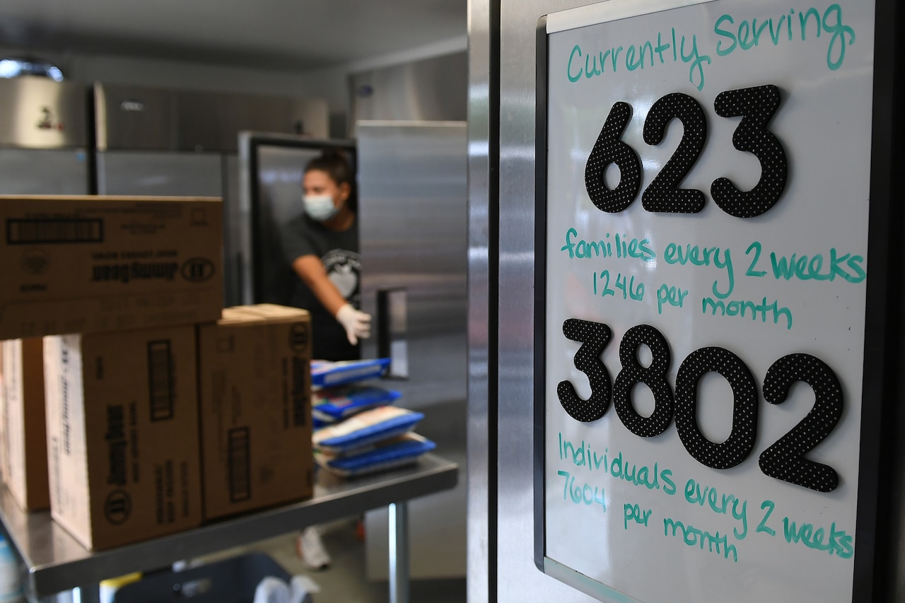 A white board shows the number of families served by a food bank as a woman works in the background.