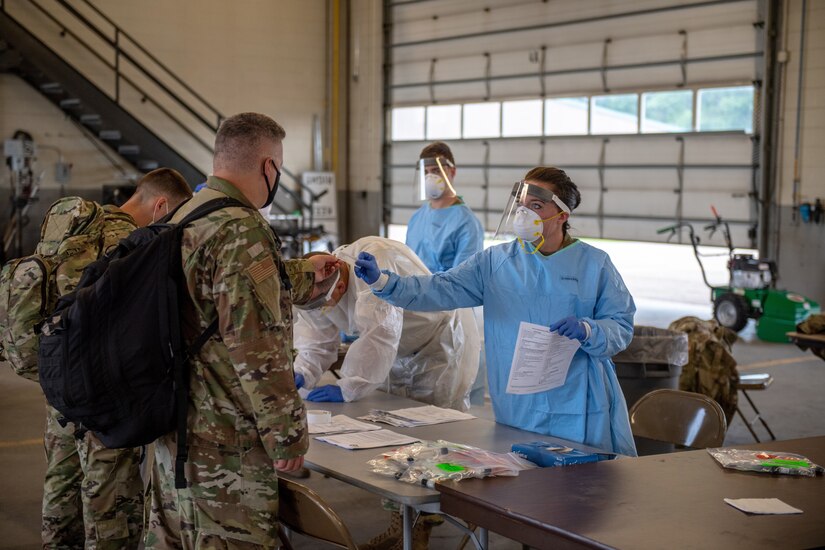 Three people dressed in protective gear test two service members wearing face masks for COVID-19.