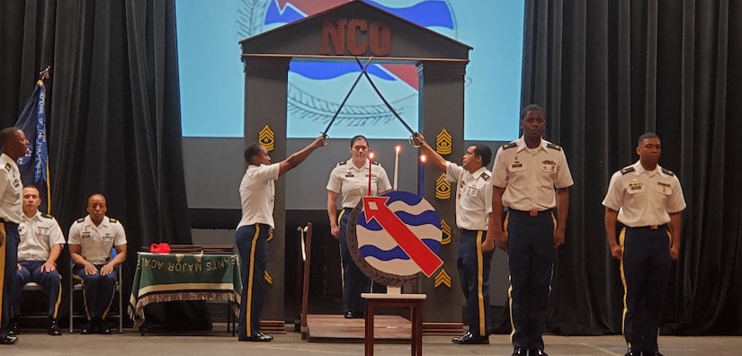 Sgt. Thea Dougher, Marine Corps Base Hawaii food inspection sergeant, walks through an arch of crossed swords to officially become a member of the NCO Corps during an NCO Induction Ceremony, March 13, 2020, in the Richardson Theater on Fort Shafter, Hawaii. Public Healthy Activity – Hawaii held their first ever NCO Induction Ceremony in conjunction with Headquarters and Headquarters Battalion. Historically, the NCO Induction Ceremony celebrates newly promoted Soldiers joining the ranks of the professional NCO Corps, while also building upon the pride all members share. (Courtesy photo)