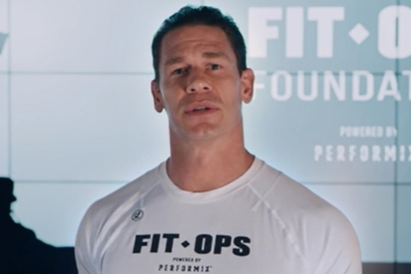 A man in a white t-shirt speaks to the camera.