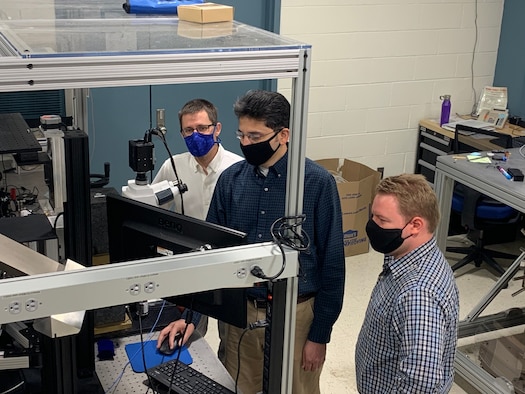 From left to right: Dr. Derek Bas, Dr. Piyush Shah and Dr. Michael Page examine a potential acoustically driven ferromagnetic resonance material under a microscope in the magneto-optics lab. The microscope is designed to observe magnetic properties on a small scale. (U.S. Air Force photo/Michael Wolf)