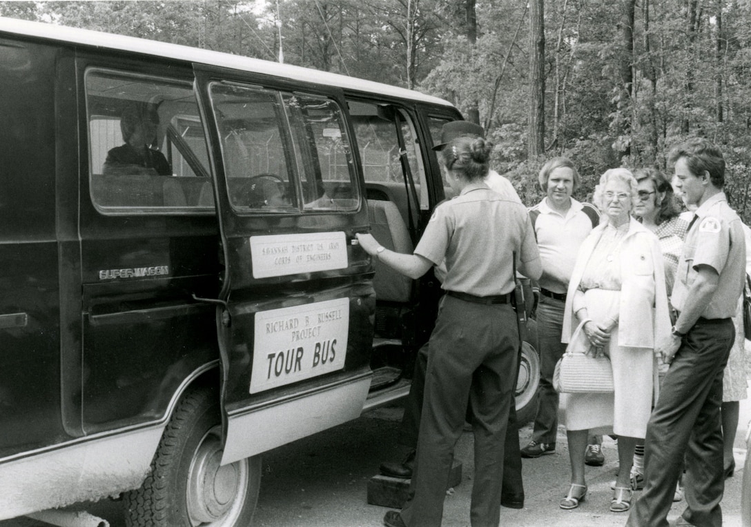 Two park rangers assist s small group of visitors into a van marked with a Tour Bus decal