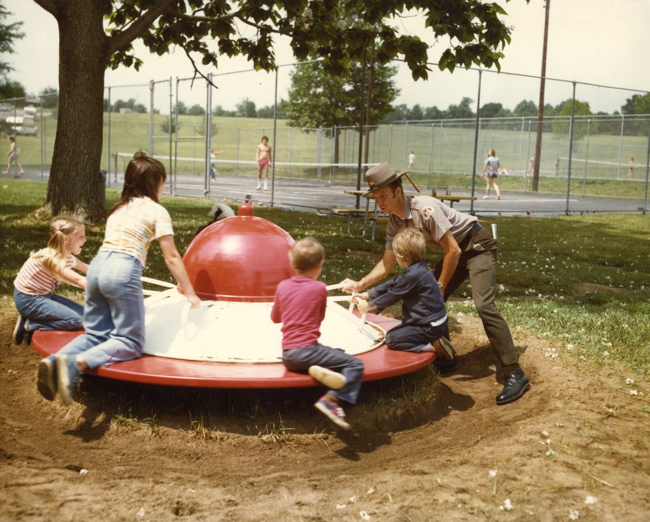 Park ranger spins children on playground equipment