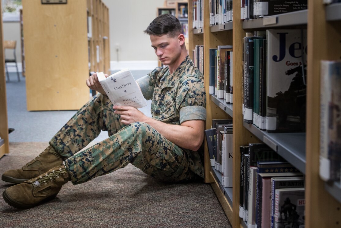 Sailor on the floor, reading a book in the library.
