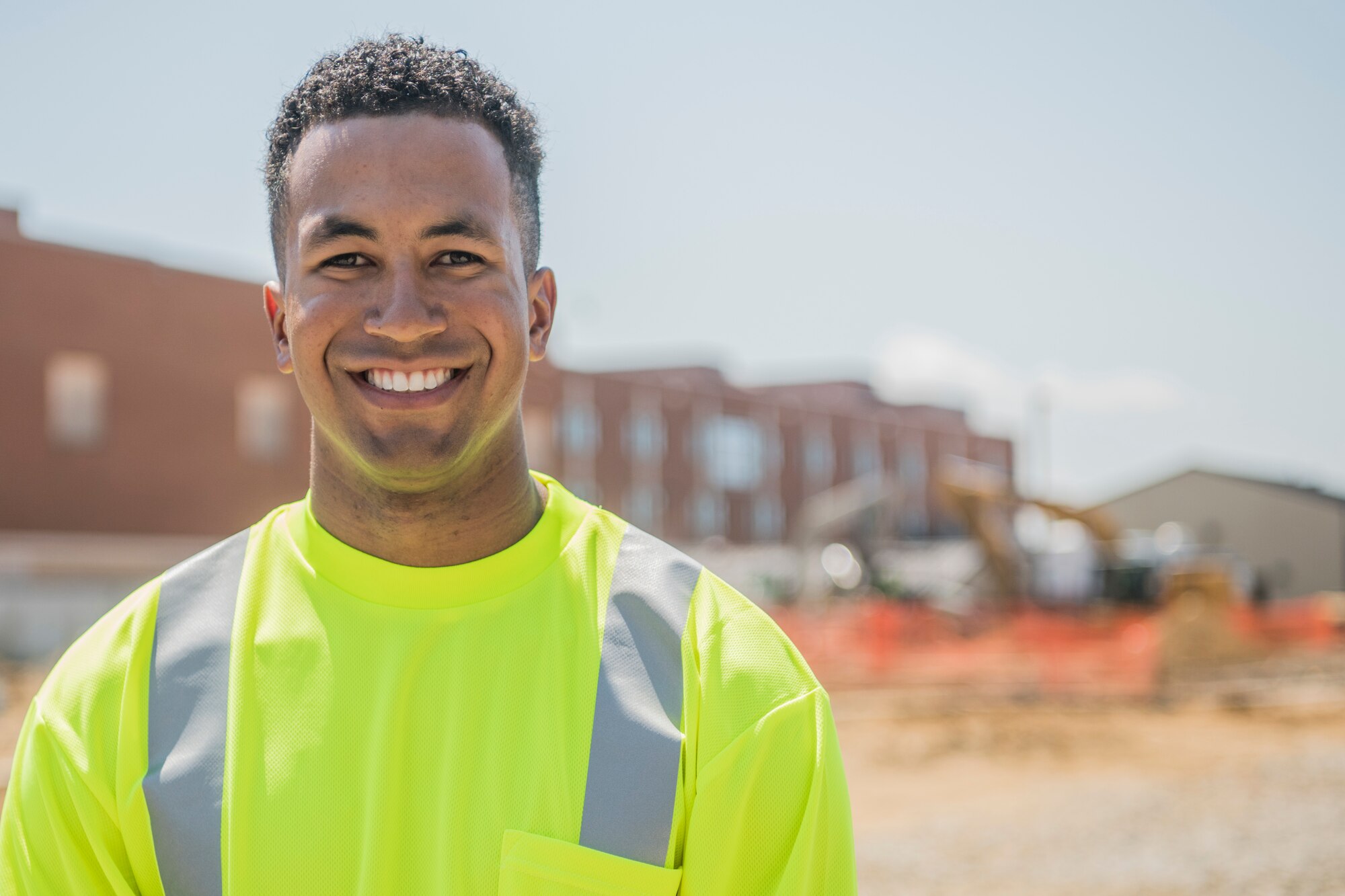 A man wearing a bright colored construction vest smiles for a photo