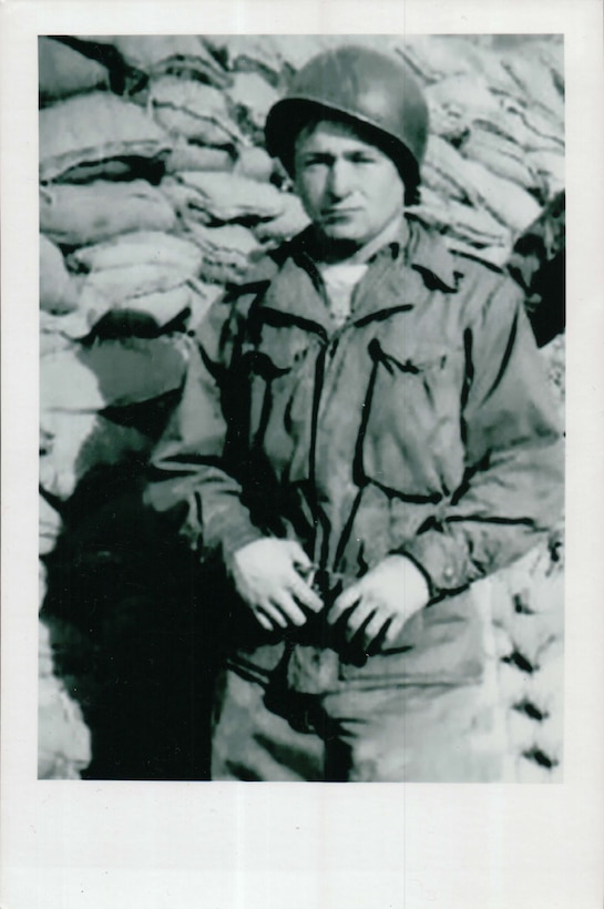 A helmet-clad soldier stands near a pile of sandbags.