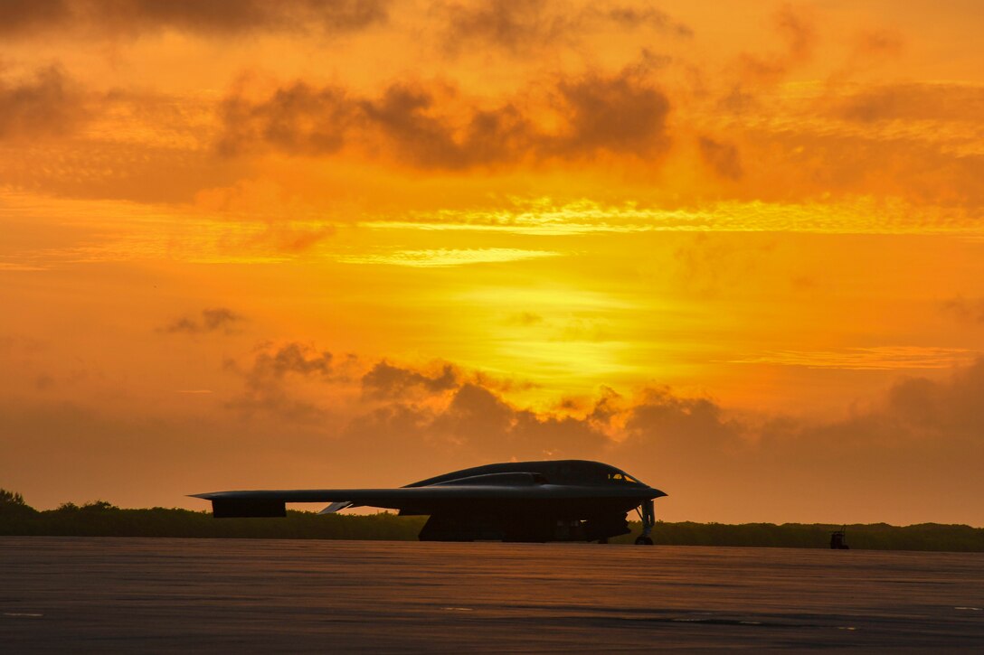 An aircraft sits under a sunlit sky on a flightline.