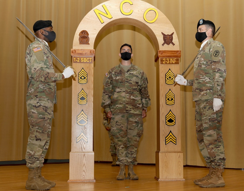 Flanked by Spc. Alloysius Odogbo, left, and Spc. Luis Ortega-Villareal, right, both assigned to Company A, Troop Battalion, Madigan Army Medical Center, Sgt. George Cordova, Company B, MAMC, goes through the arch at the NCO induction ceremony at Joint Base Lewis-McChord, Wash., Aug. 7, 2020. (Photo Credit: Christopher Larsen)