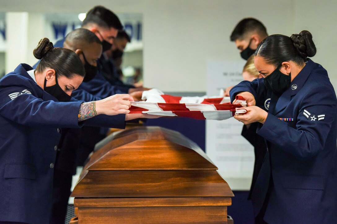 Service members fold an American flag over a casket.