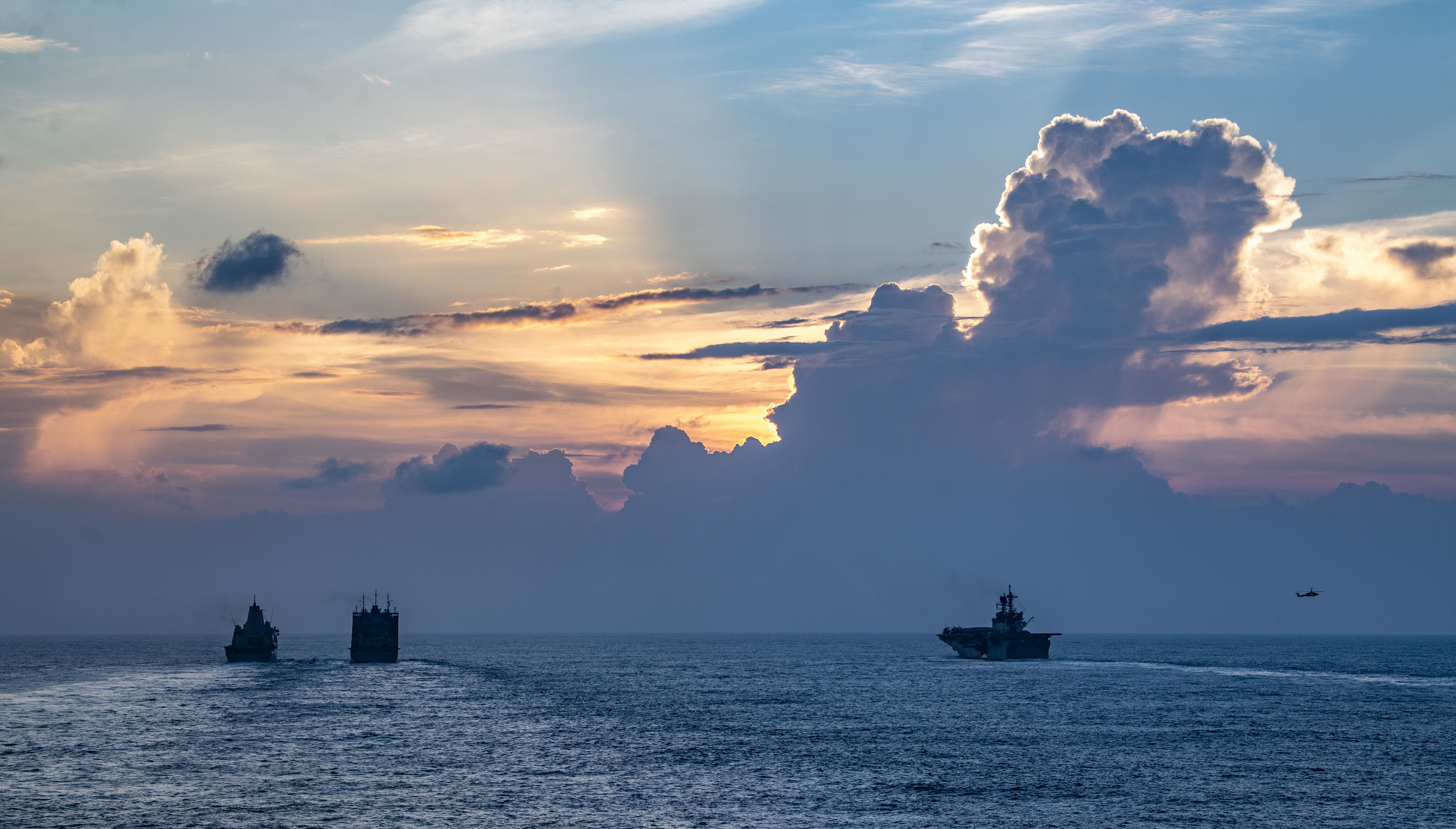 USS New Orleans (LPD 18), left, and USS America (LHA 6), right, conduct a replenishment-at-sea with USNS Charles Drew (T-AKE 10) with MH-60S Sea Hawk helicopters.