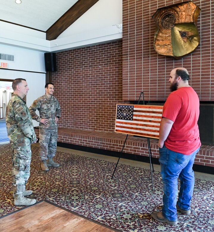 Brandon Champion, right, an Arnold Engineering Development Complex (AEDC) instrumentation technician, speaks with AEDC Commander Col. Jeffrey Geraghty, center, and AEDC Superintendent Chief Master Sgt. Robert Heckman about the artistic representation of a flag he made and gifted to the Air Force, Aug. 7, 2020, at Arnold Lakeside Center at Arnold Air Force Base, Tenn. Champion gifted the flag in recognition of the AEDC response to the COVID-19 pandemic. (U.S. Air Force photo by Jill Pickett)