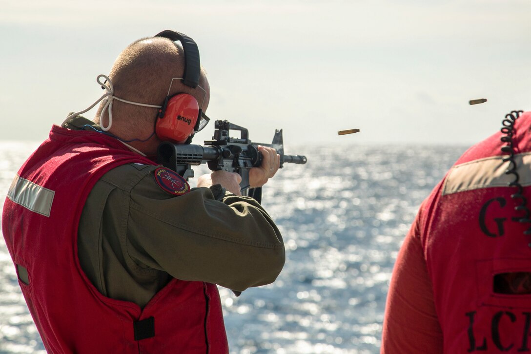 A sailor fires a weapon from the deck of a ship on the ocean.