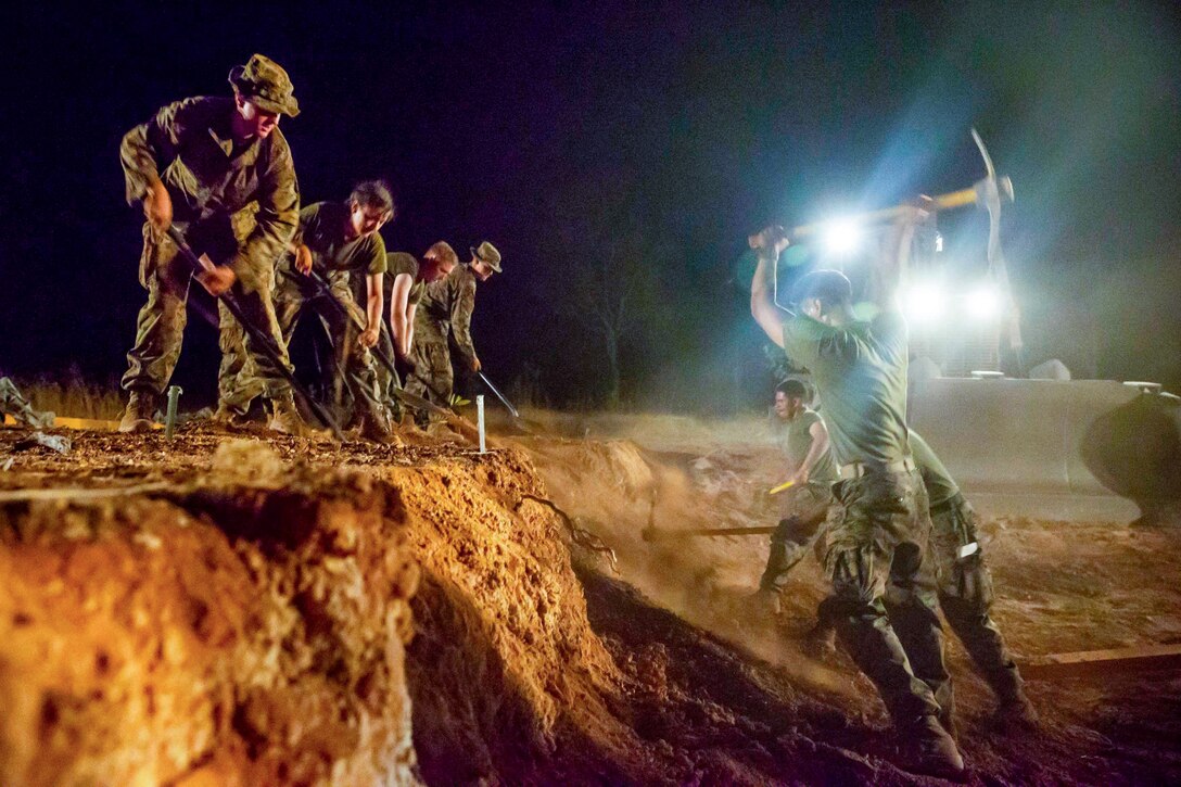 Marines dig in the dark with spotlights above them.