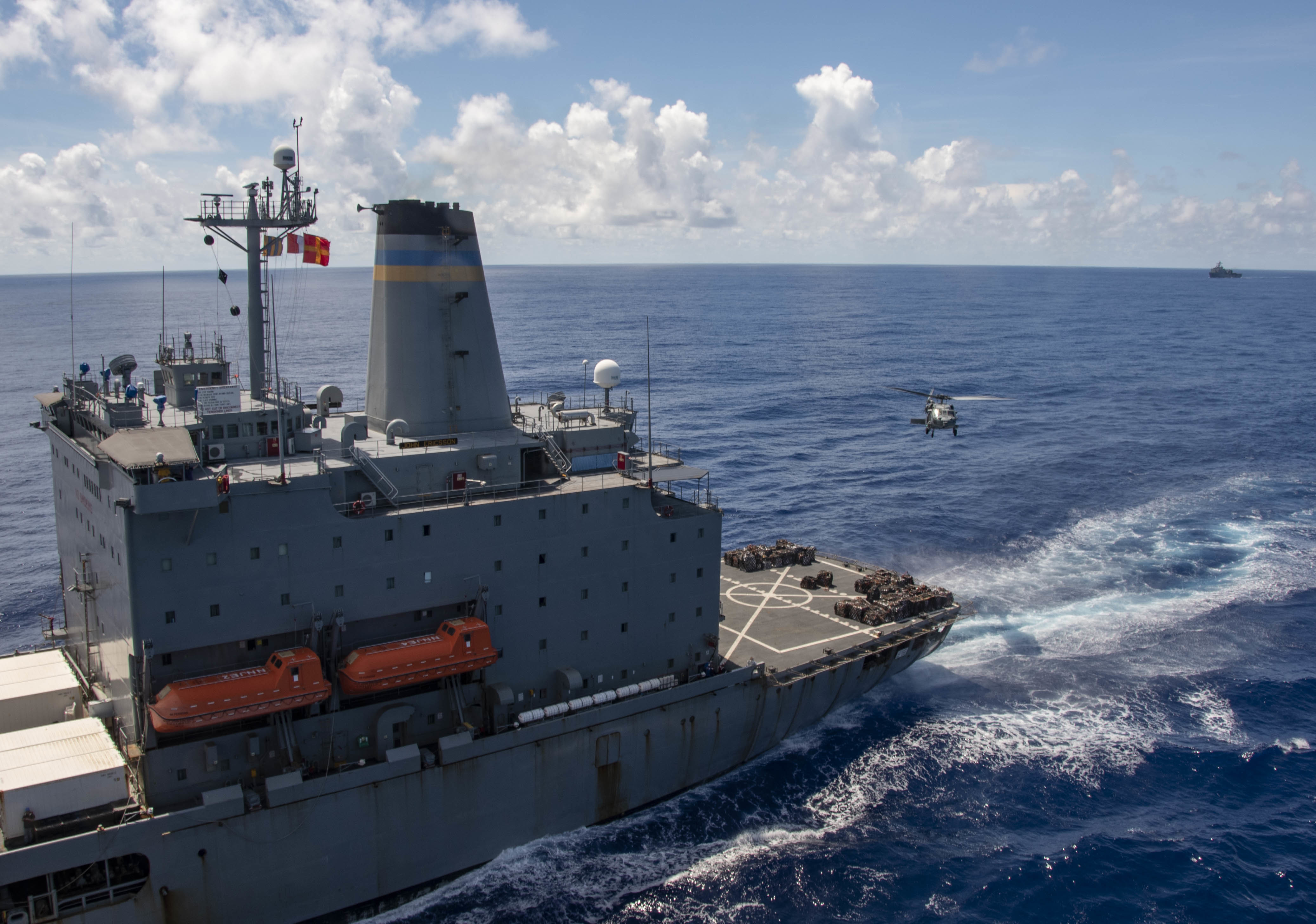 An MH-60S Sea Hawk, attached to the "Golden Falcons" of Helicopter Sea Combat Squadron (HSC) 12, transports cargo during a replenishment-at-sea with fleet replenishment oiler USNS John Ericsson (T-AO 194), left, and the Navy's only forward-deployed aircraft carrier USS Ronald Reagan (CVN 76) as the amphibious dock landing ship USS Comstock (LSD 45) steams behind.
