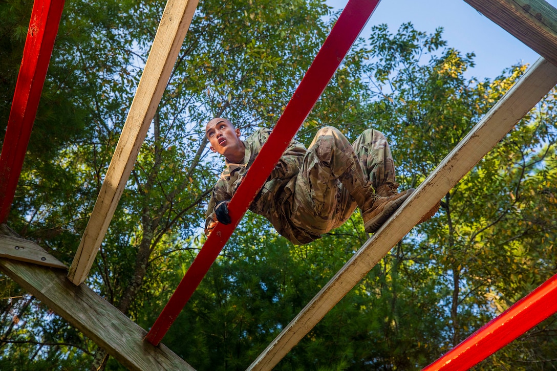A soldier climbs up a wooden obstacle with red and unpainted planks.