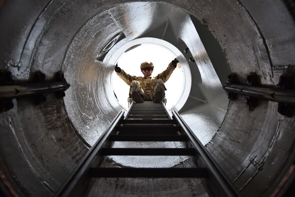 An Airman stands on a ladder and looks down a shaftway into a launch facility.