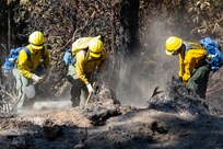 Three soldiers in firefighting gear dig in the dirt.