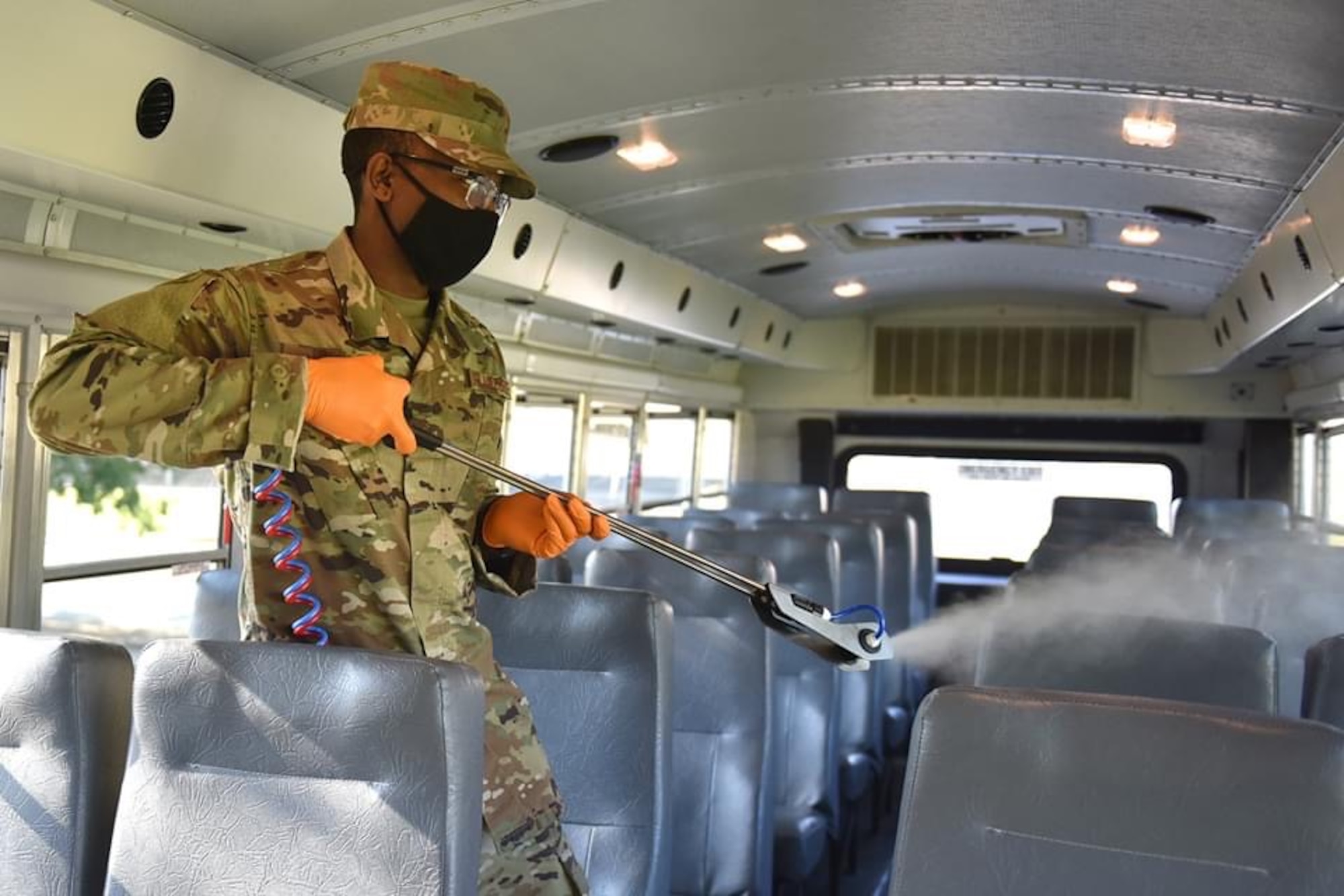Photo shows an Airman spraying disinfectant on seats inside a bus.