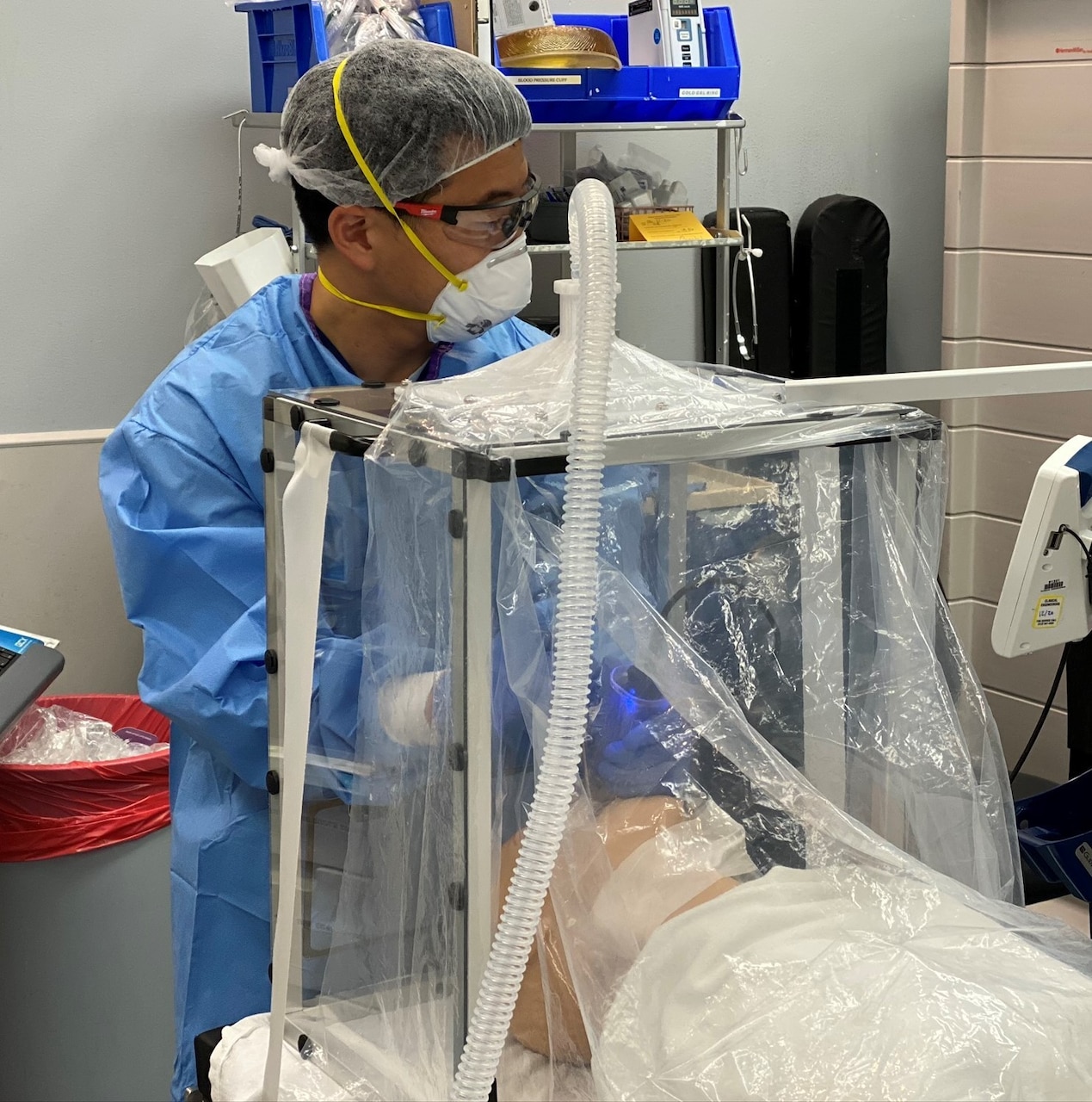 A man in full medical protective gear works with a simulated patient in a biocontainment unit.