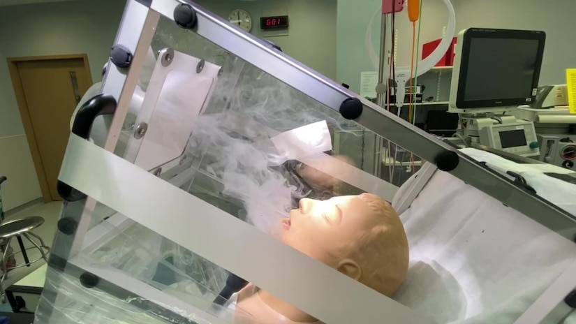 A simulated COVID patient is enclosed in a biocontainment unit.