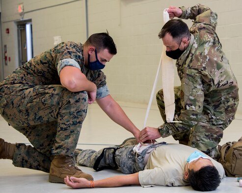 Two service members are bandaging a wound on a simulated injured service member.