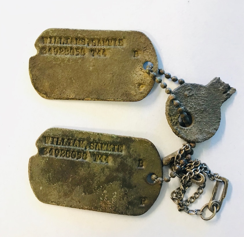Two rusted dog tags are attached to a short chain and a broken key.