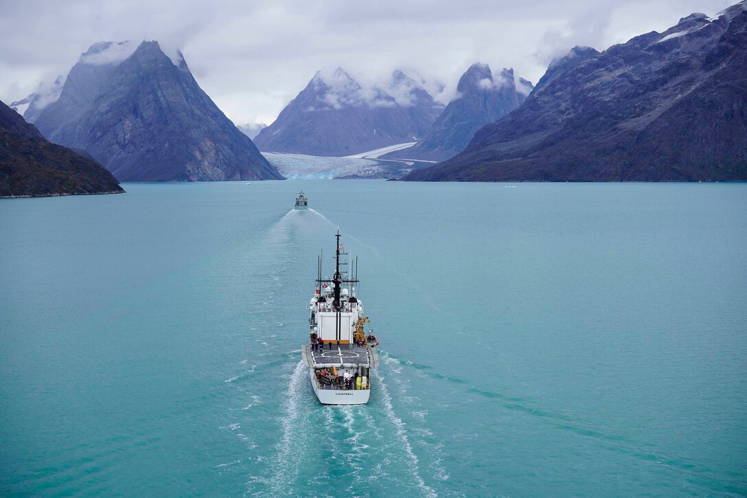 A Coast Guard cutter travels in waters surrounded by mountain peaks.