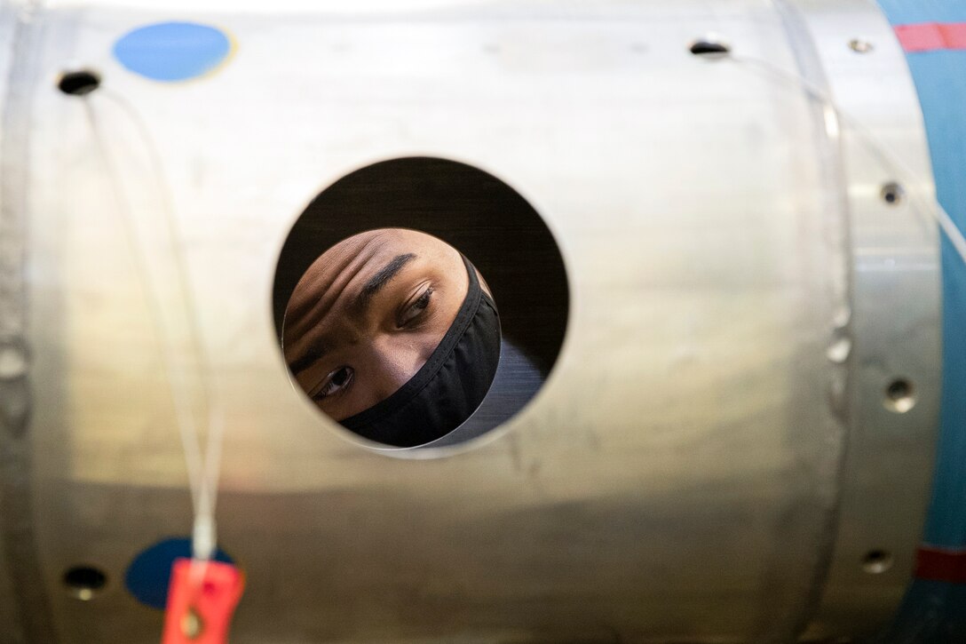 A sailor's face is visible through a circular opening on a section of a mine.