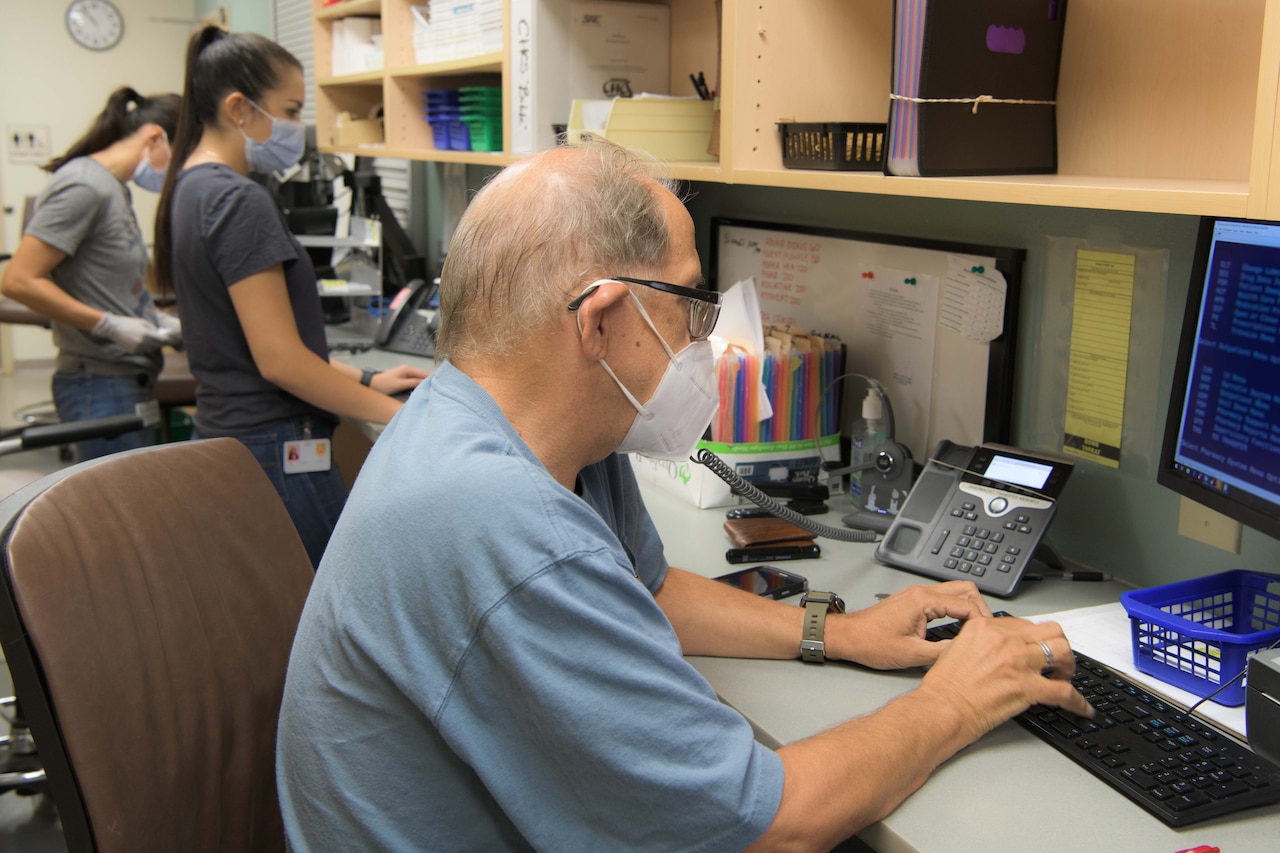 A man wears a face mask while working on a computer.