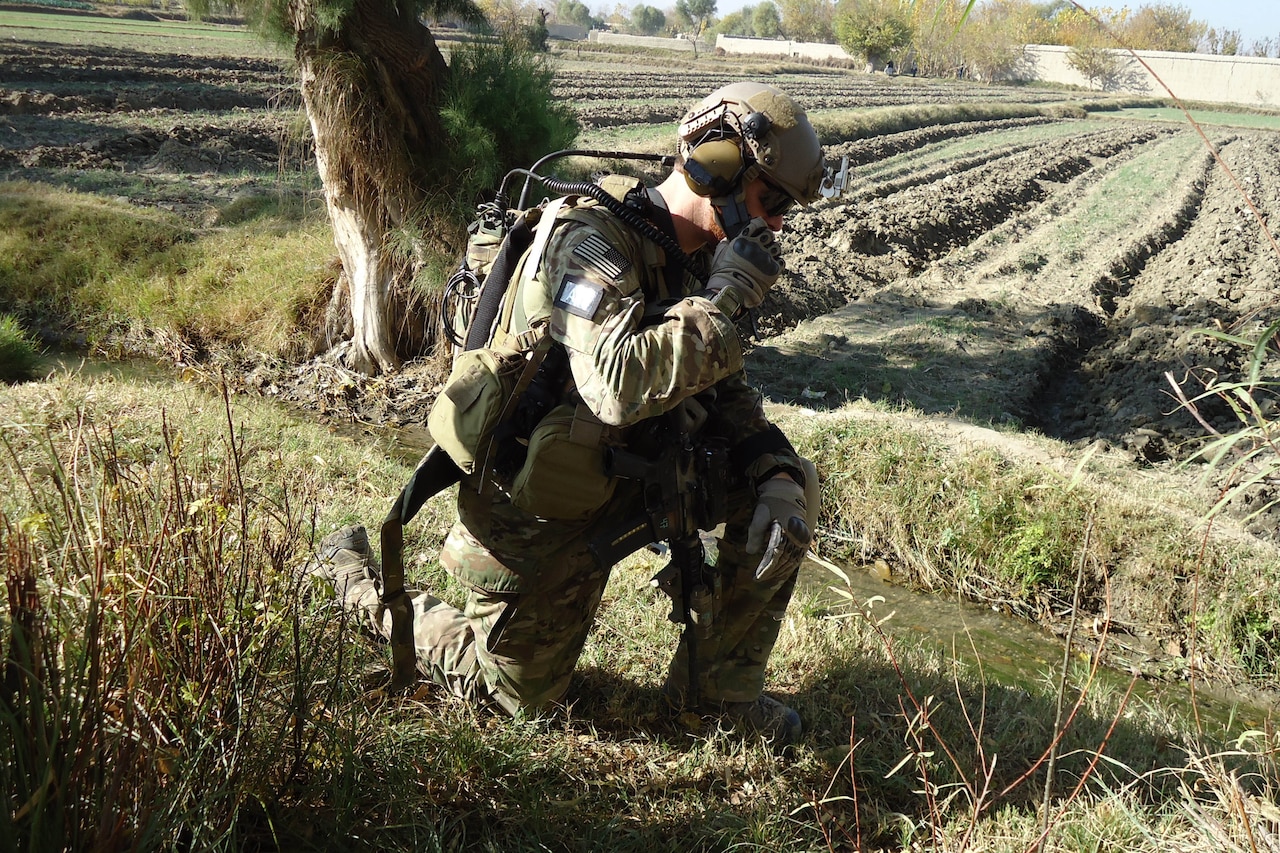 A soldier is down on one knee in a field.