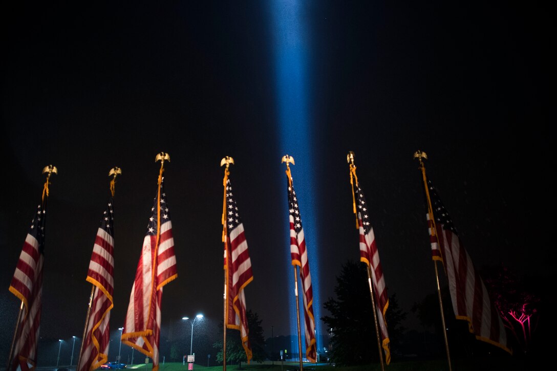 A blue pillar of light illuminates the night sky over a display of American flags.