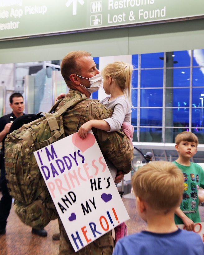MSgt. Bryce Weight, an Alaska Air Guardsmen with the 176th Security Forces Squadron, holds his daughter with her welcome home sign in hand, at Ted Stevens-Anchorage International Airport upon his return from Kandahar, Afghanistan on June 22, 2020. 12 AKNG Airmen deployed in support of Operation Freedom Sentinel, a NATO-led continuation of the Global War on Terrorism. (U.S. Air National Guard photo by Lt. Col. Candis Olmstead/Released)