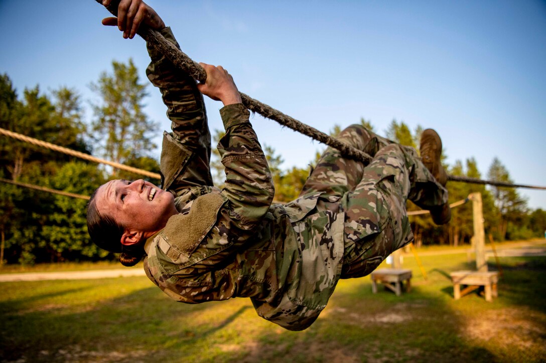 A soldier pulls herself along a rope.