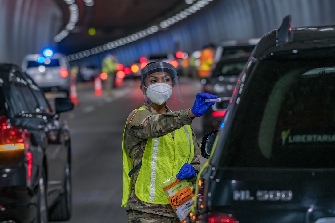 A guardsman helps administer a COVID-19 test to someone in a car stopped on the roadway.