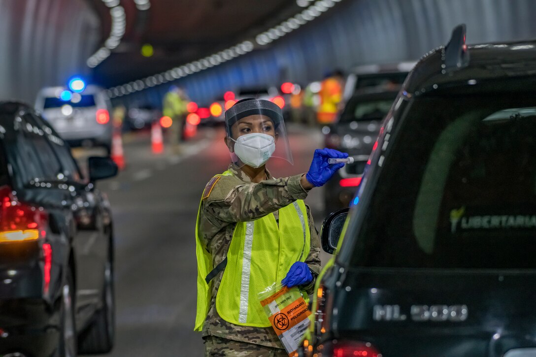 A soldier shows a vial to motorist while on a roadway.