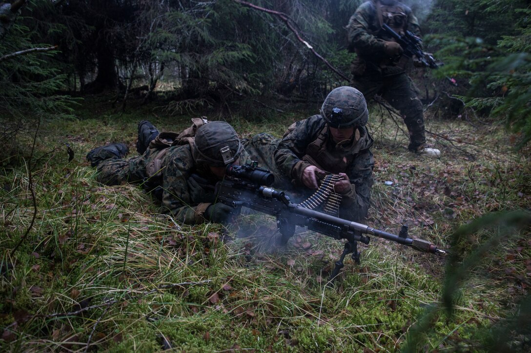 Two Marines lie on the ground and fire machine guns.