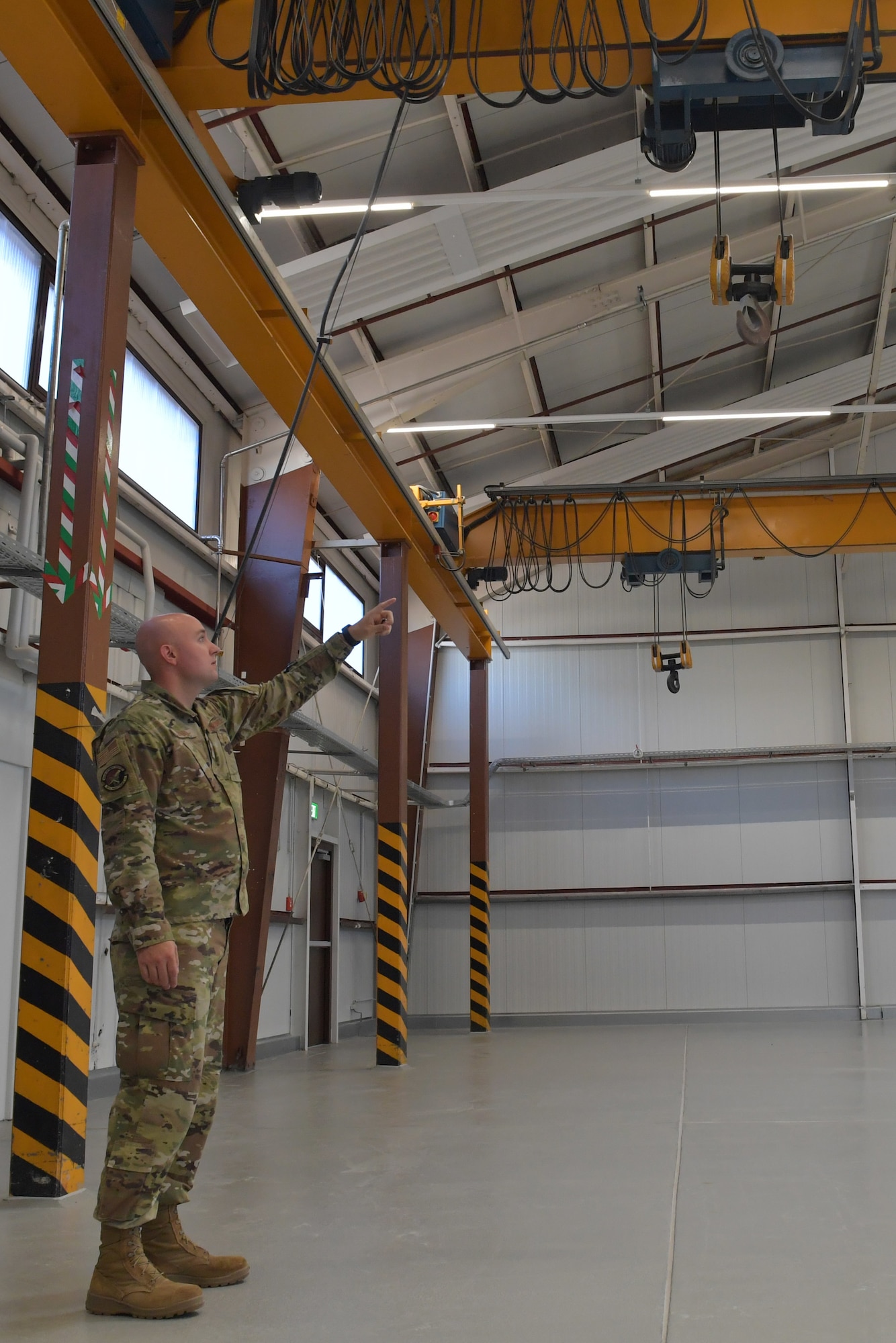 An Airman points to a hoist hanging in a maintenance facility.